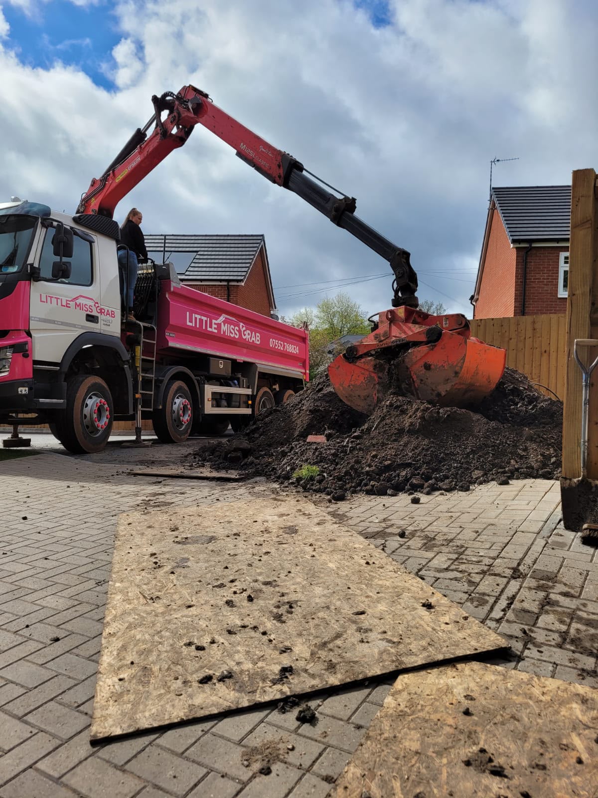 Little Miss Grab lorry scooping muck and soil pile on a residential block paved driveway