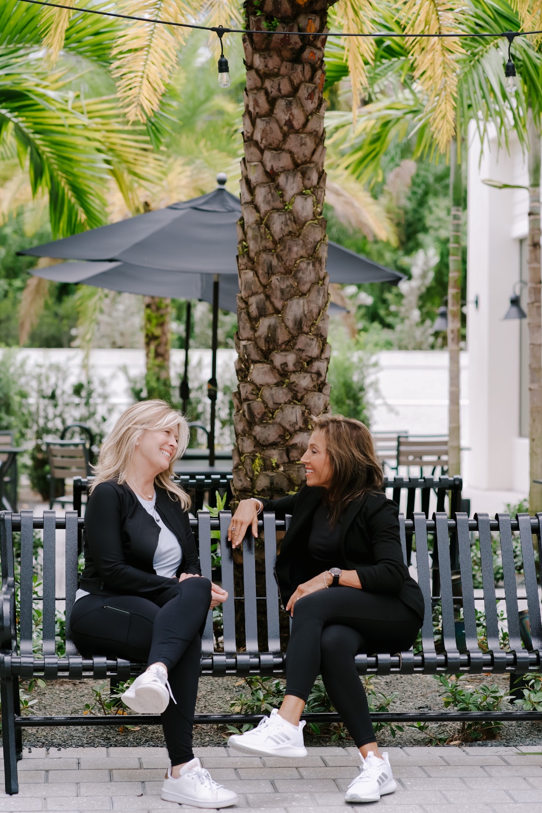 Lori laughing with a client on a bench under palm trees