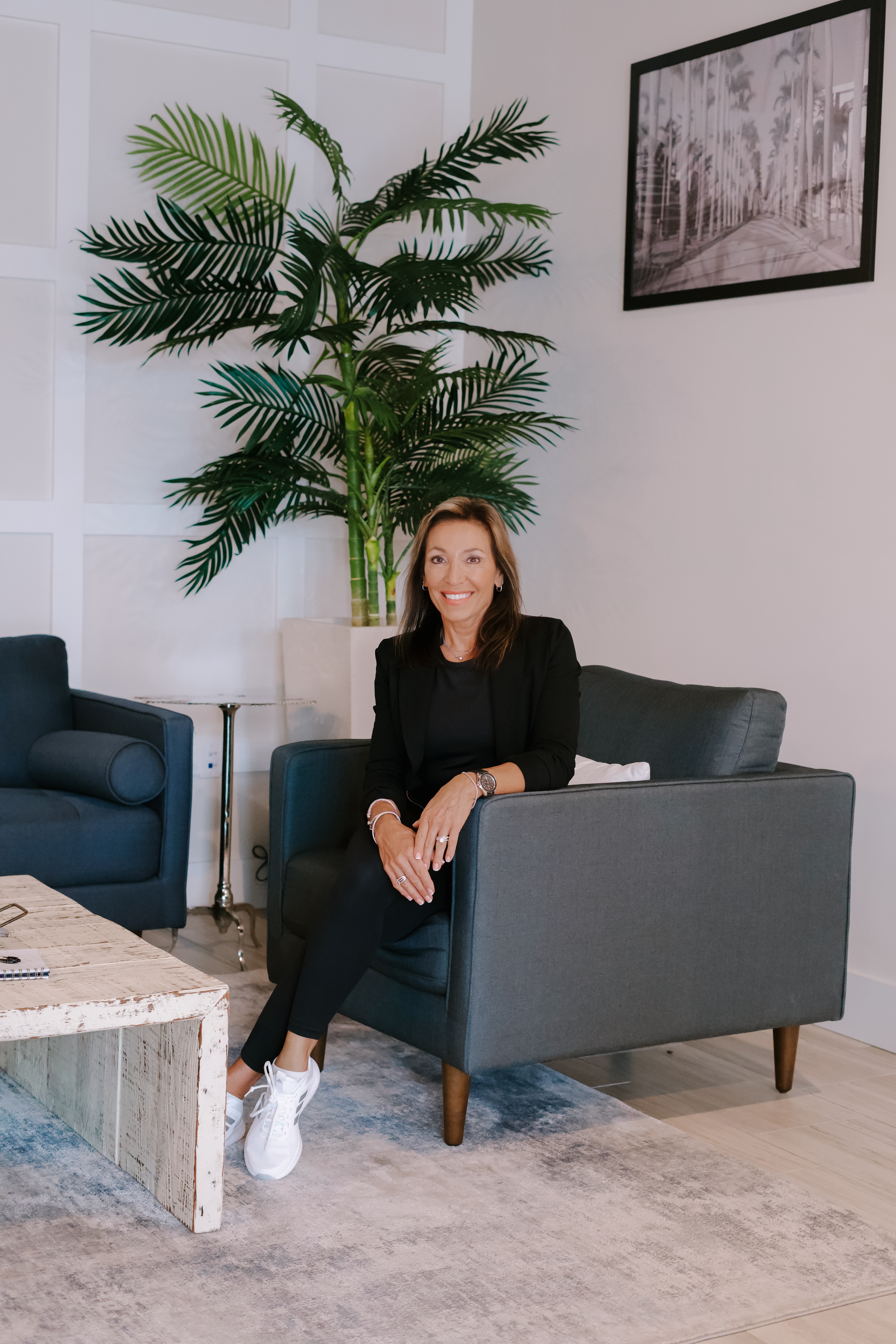 Lori Nolan seated in an armchair in a bright studio with palm plant
