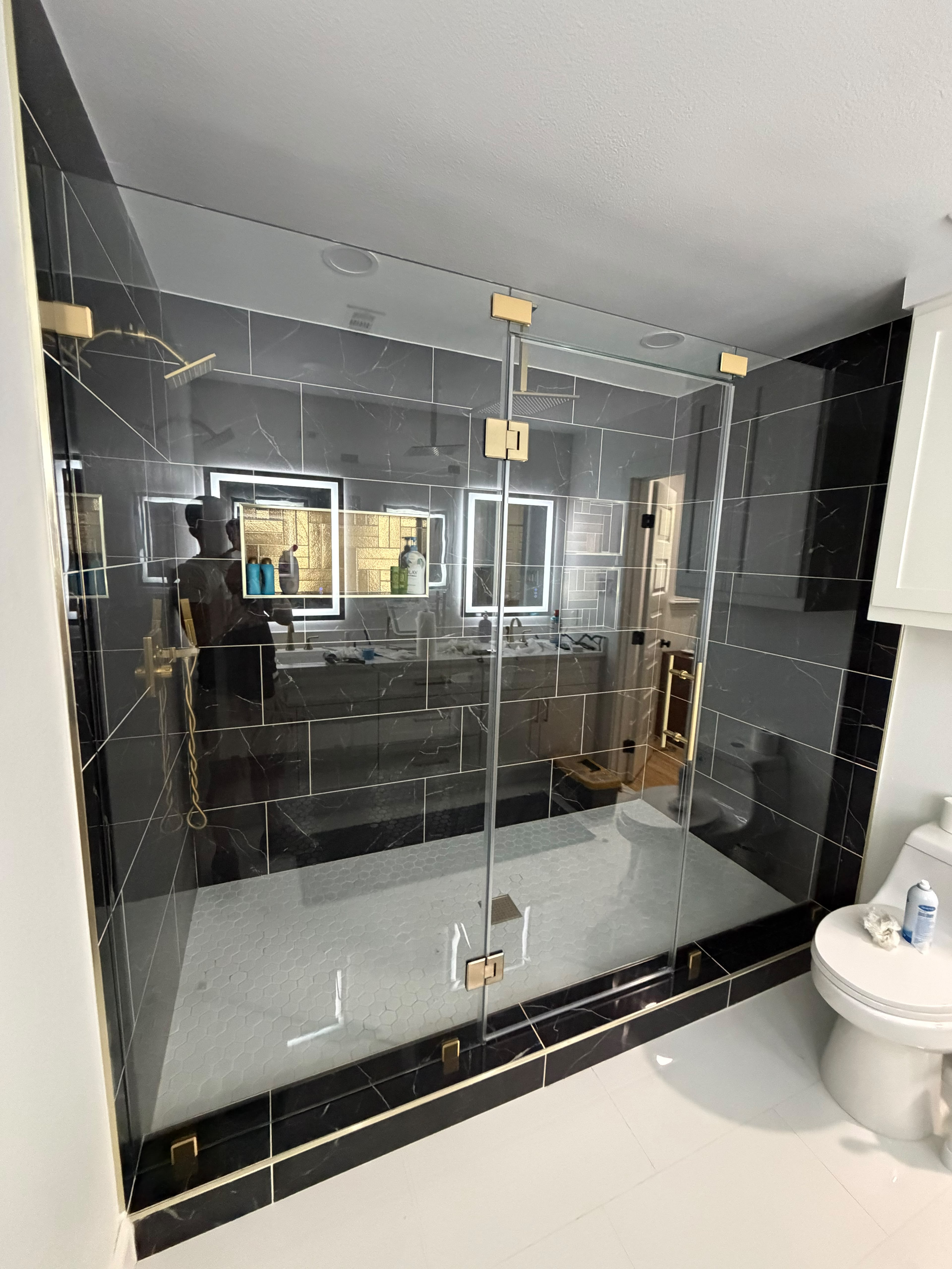 Custom frameless glass shower enclosure on black marble with brushed gold hardware