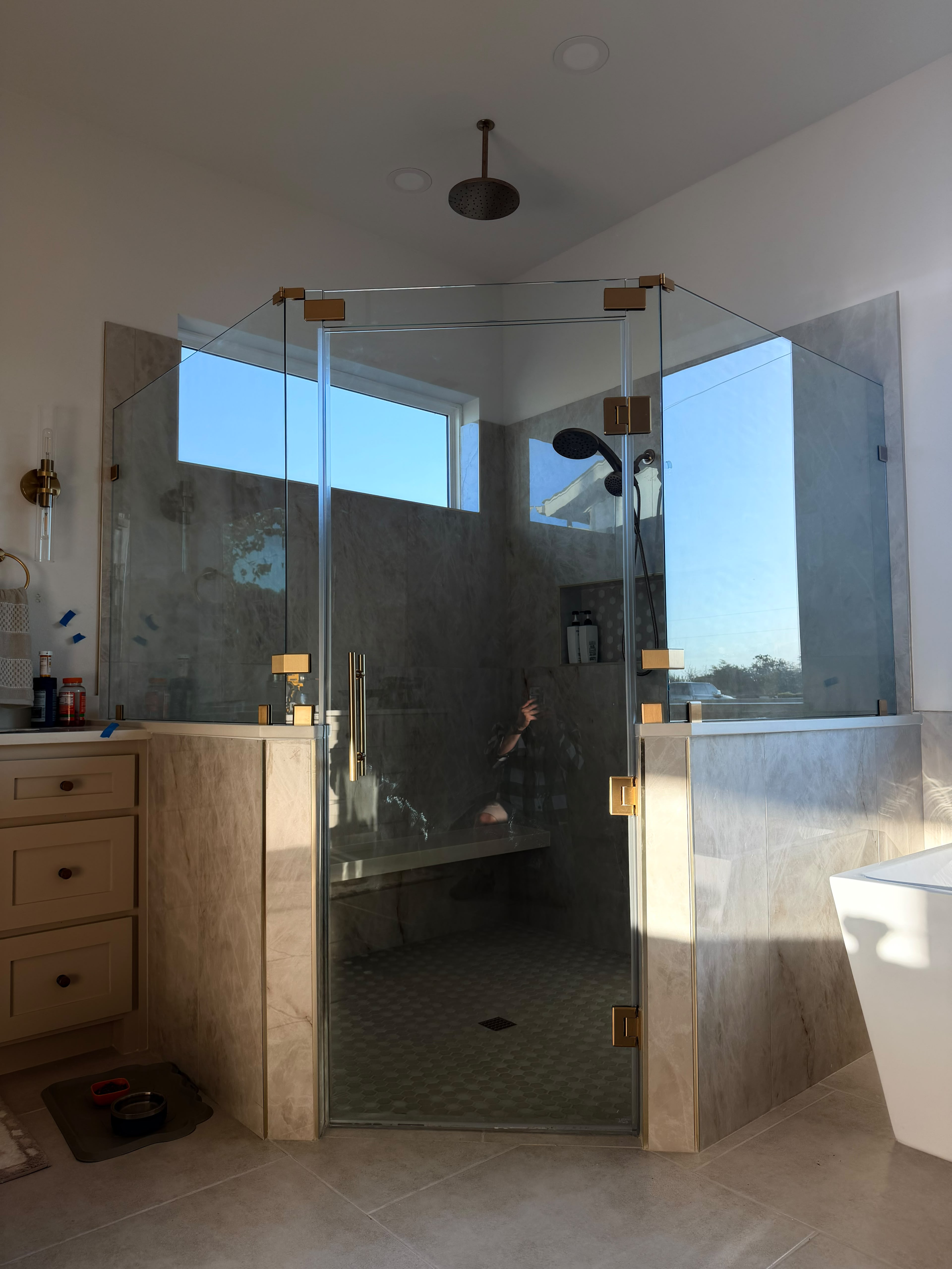 Custom neo-angle glass shower enclosure over pony wall with satin gold clamps and bench