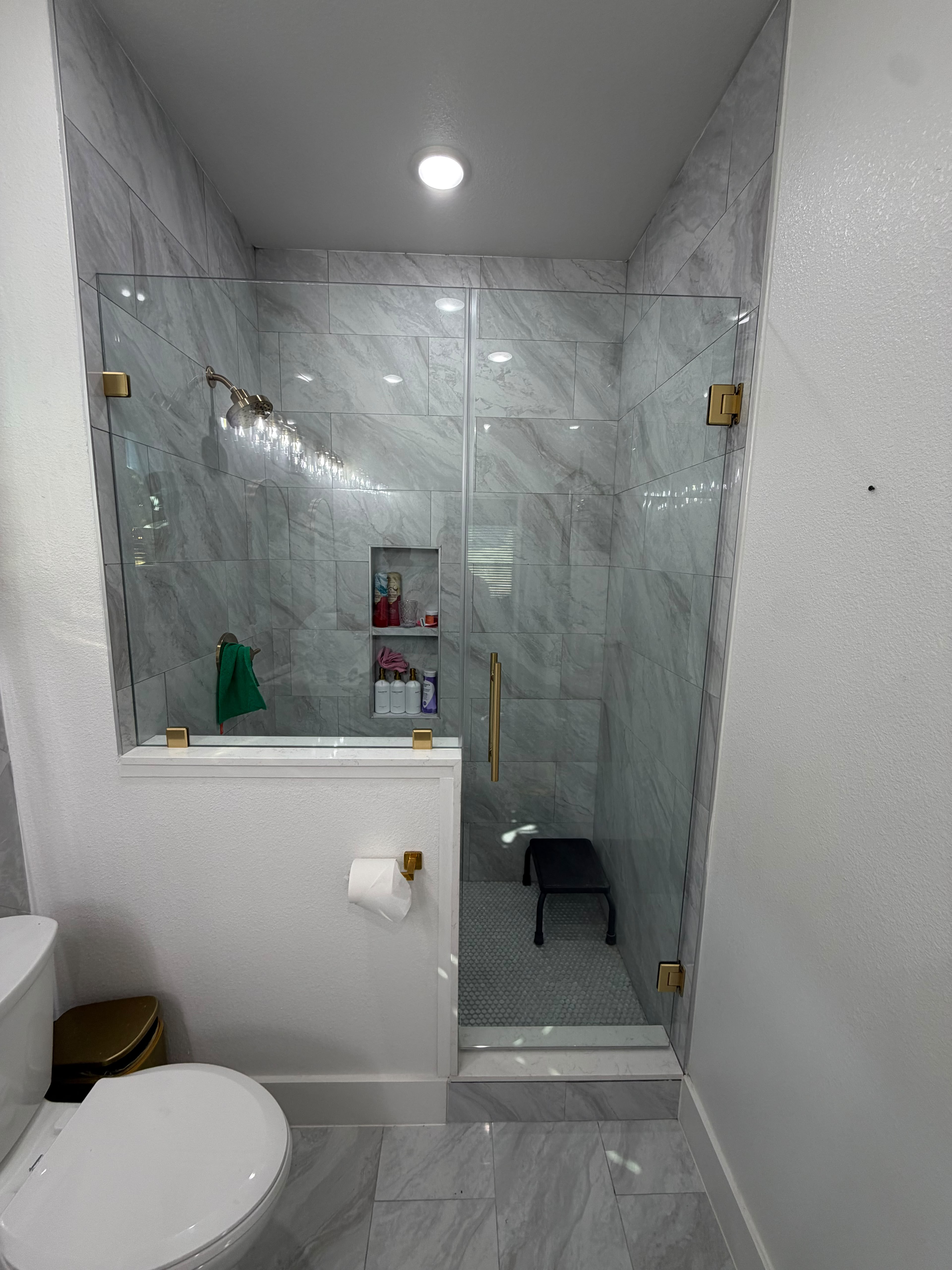 Frameless glass shower door and panel on half wall with gold hardware