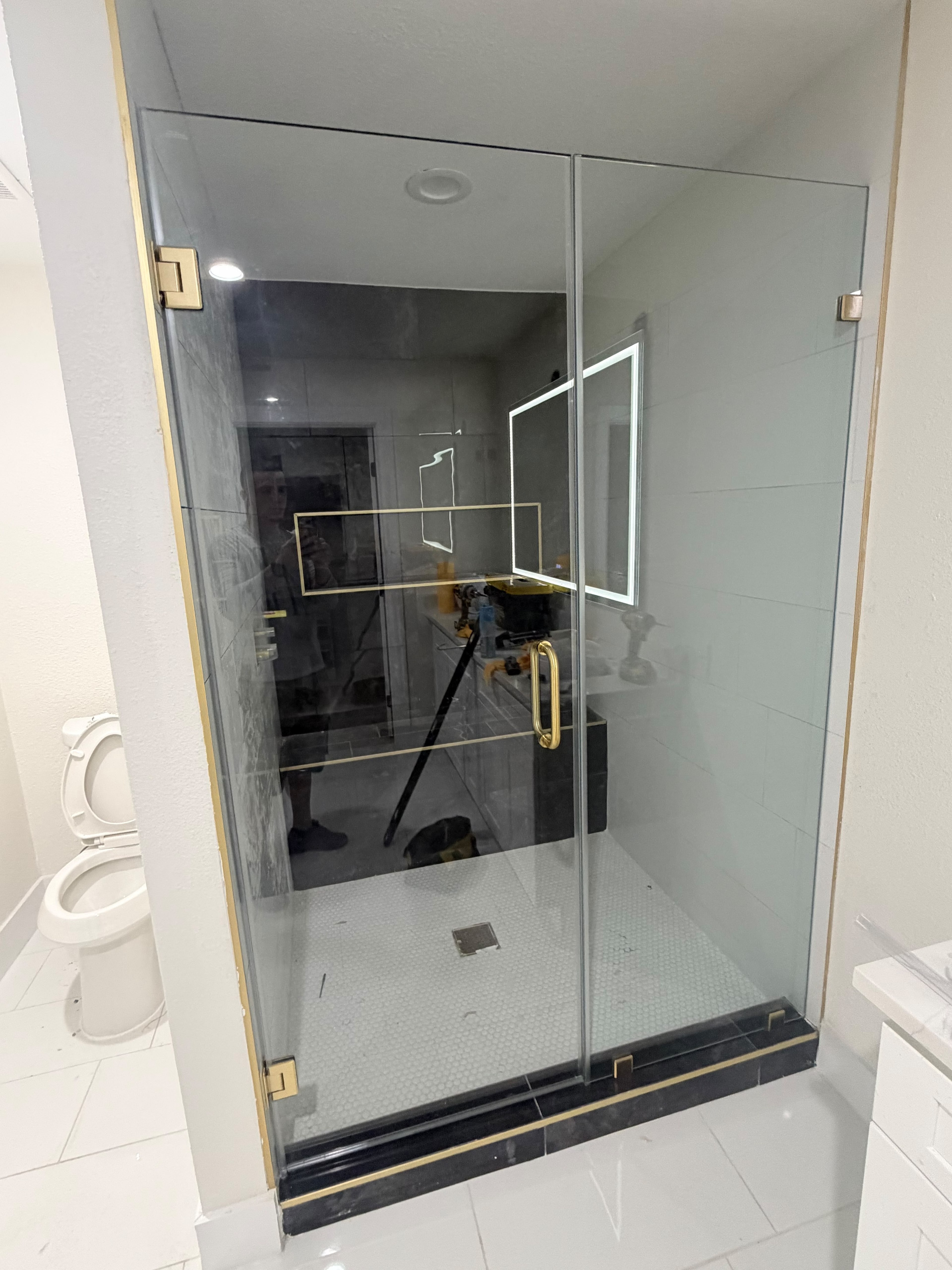 Modern frameless glass shower enclosure with satin brass hardware and illuminated vanity