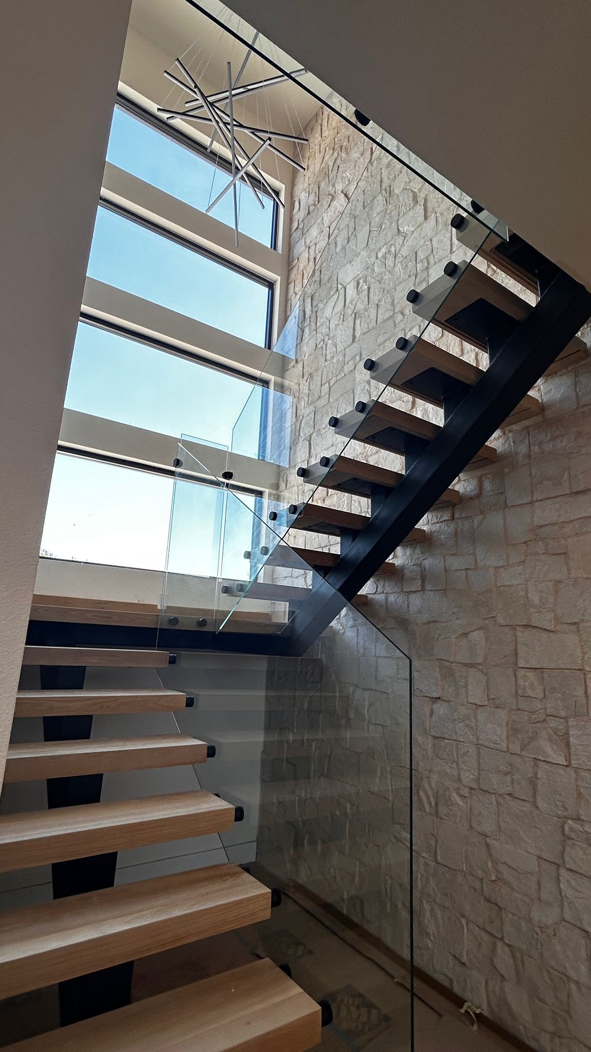 Floating wood tread staircase with custom glass panel railing and stone wall
