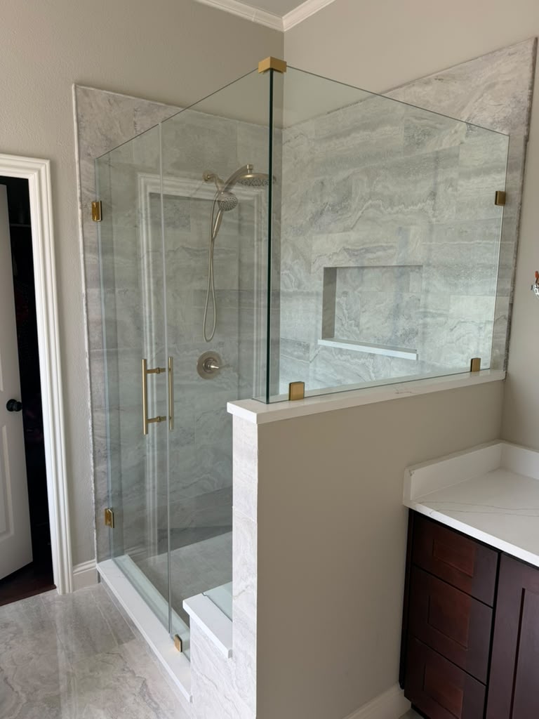 Frameless glass shower enclosure on half-wall with brushed gold clamps and bench