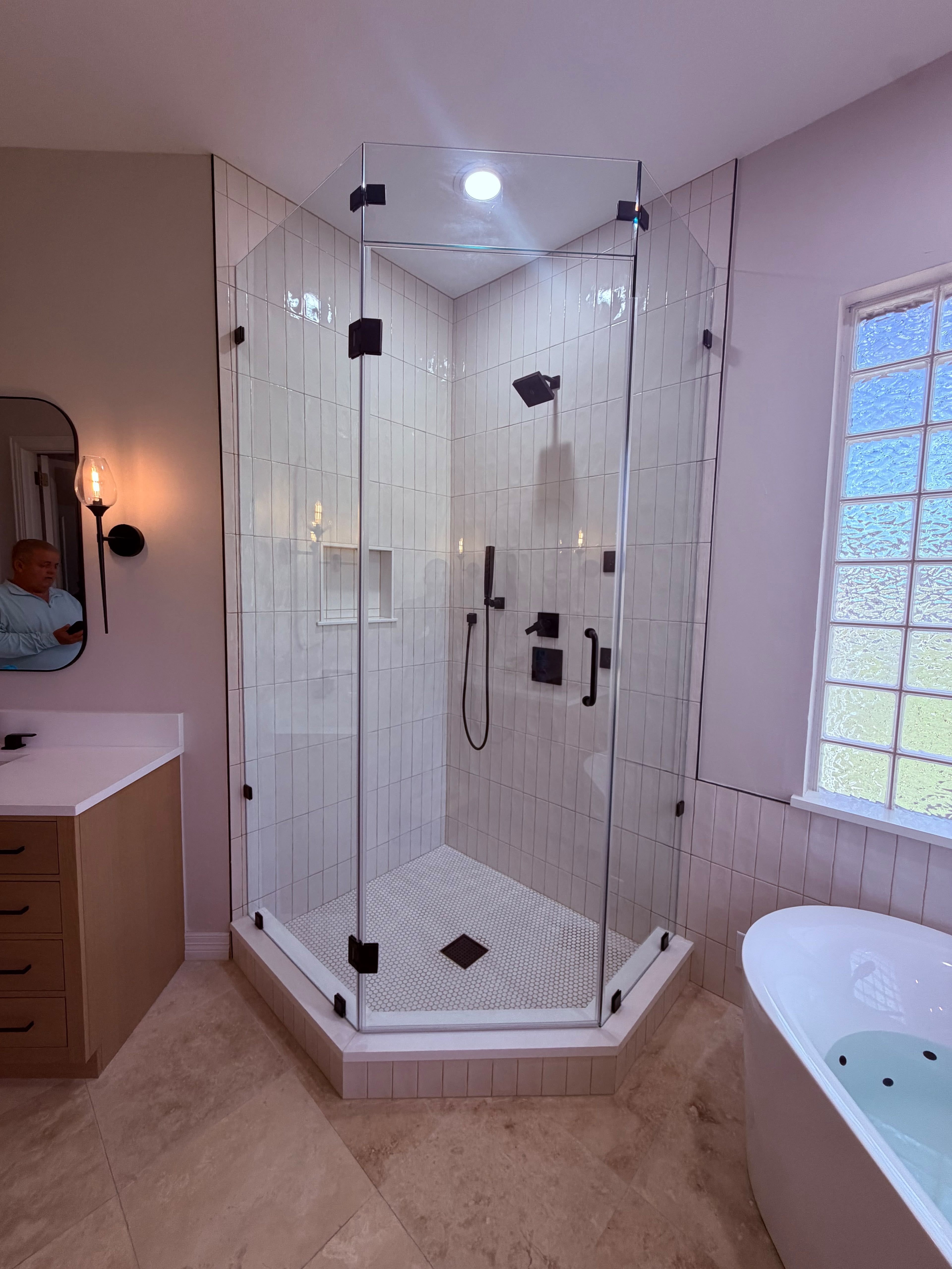 Custom neo-angle frameless shower enclosure with matte black hardware and mosaic floor tile