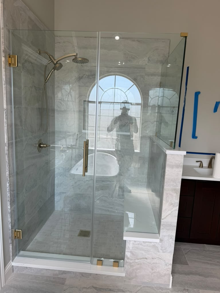 Frameless glass shower enclosure on half-wall with brushed gold hardware and tiled bench