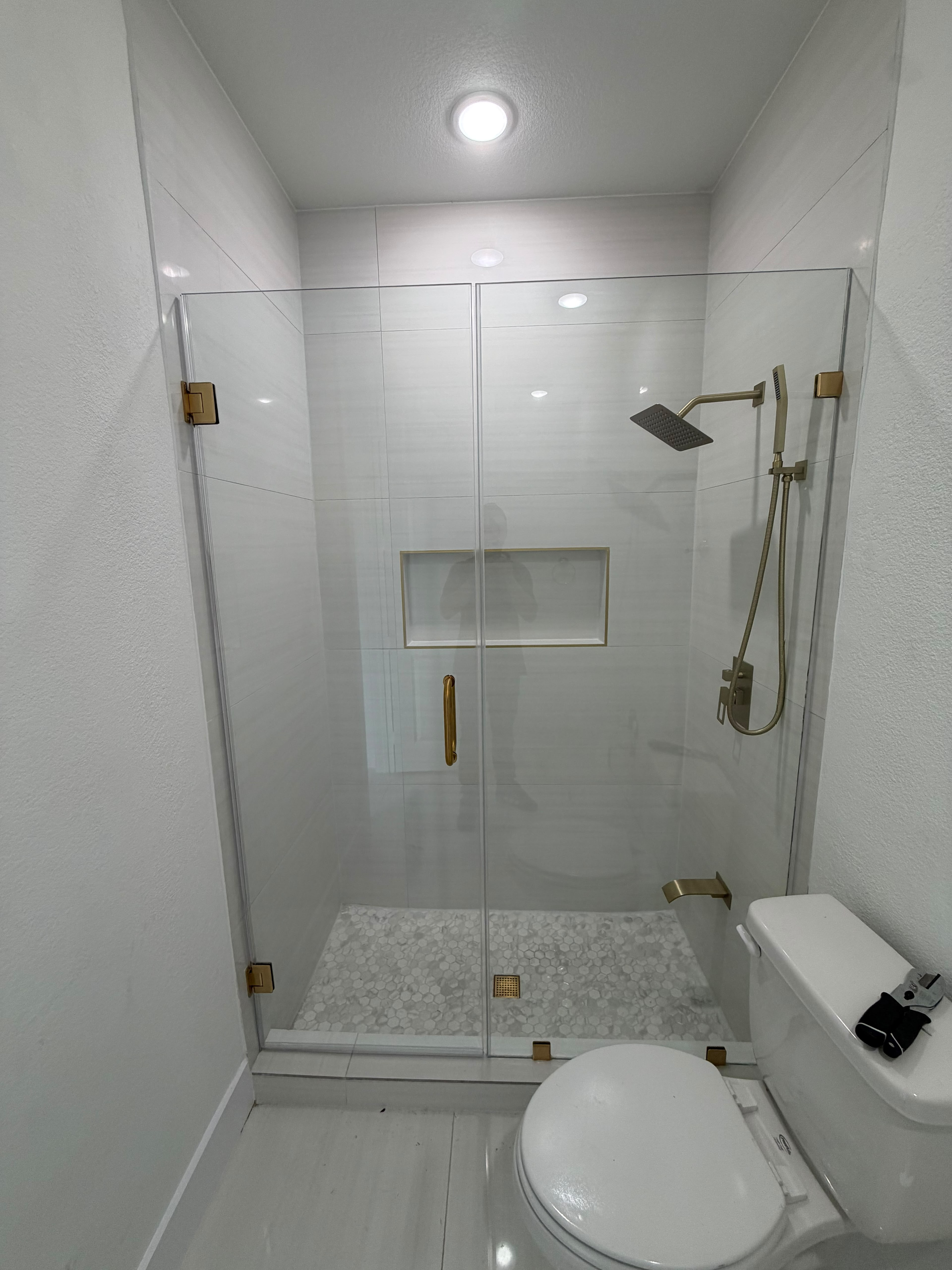 Frameless sliding glass shower door with gold hardware