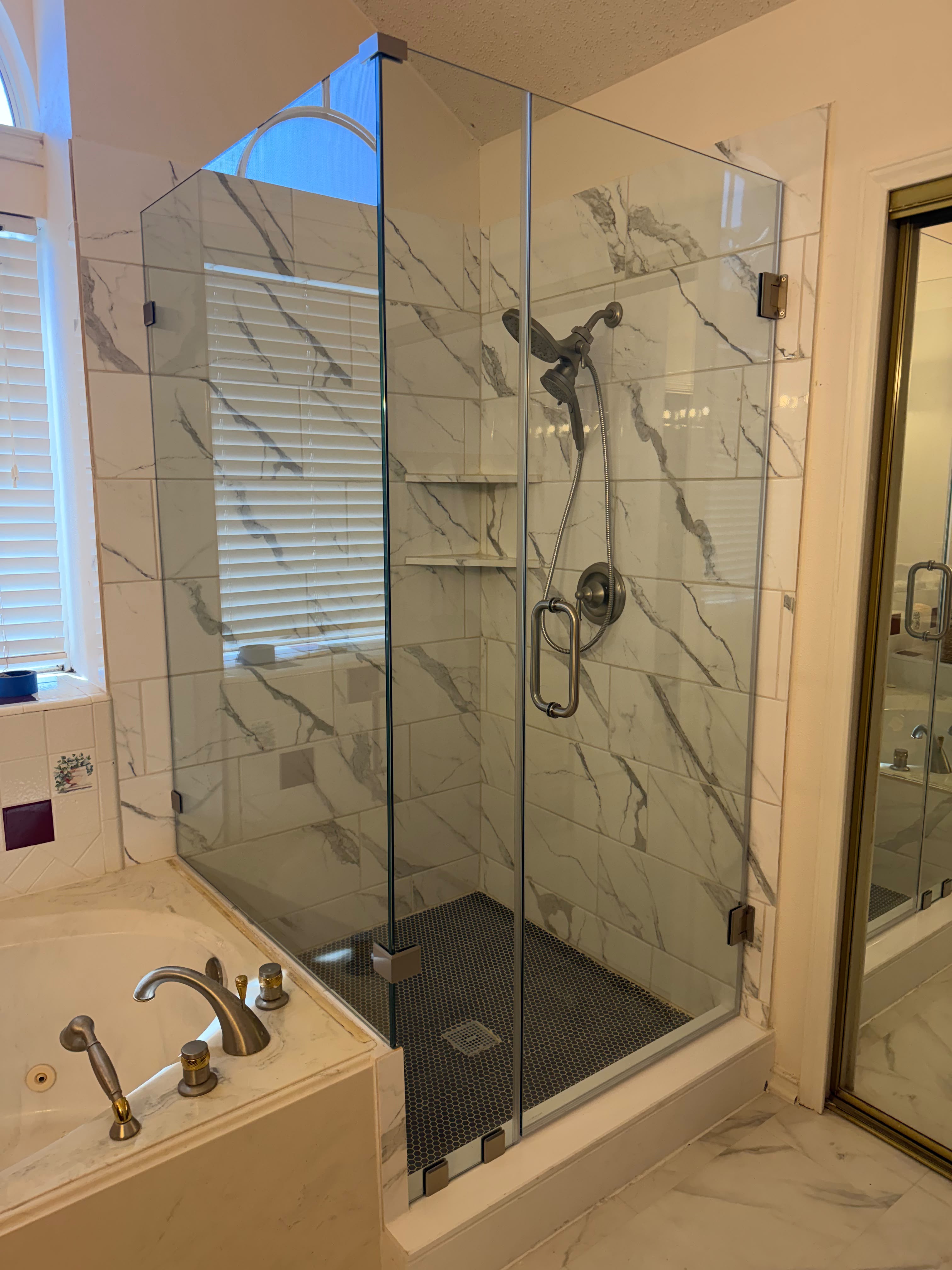 Frameless corner glass shower enclosure next to bathtub with brushed nickel hardware