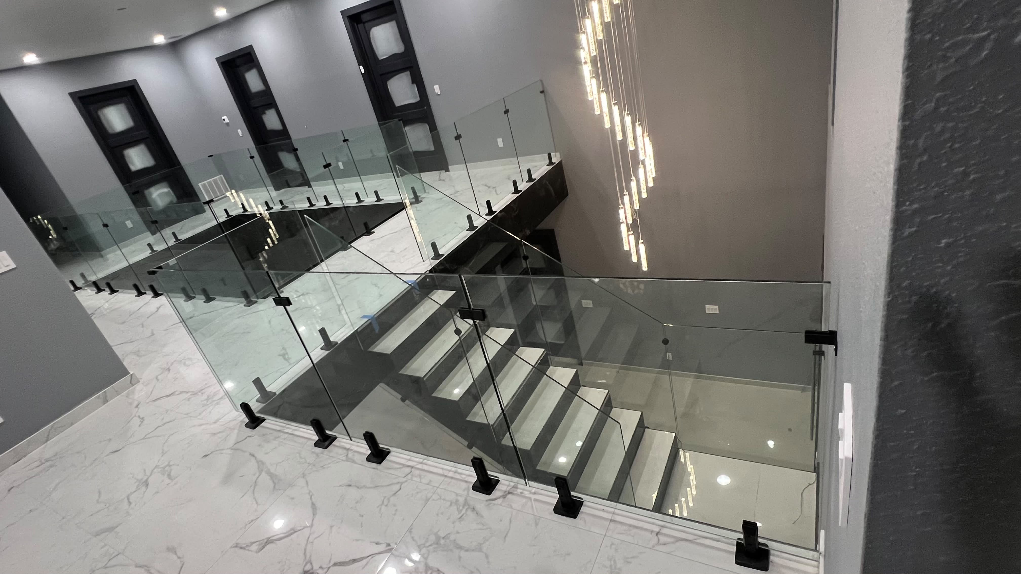 Custom interior glass stair railing with matte black clamps and chandelier