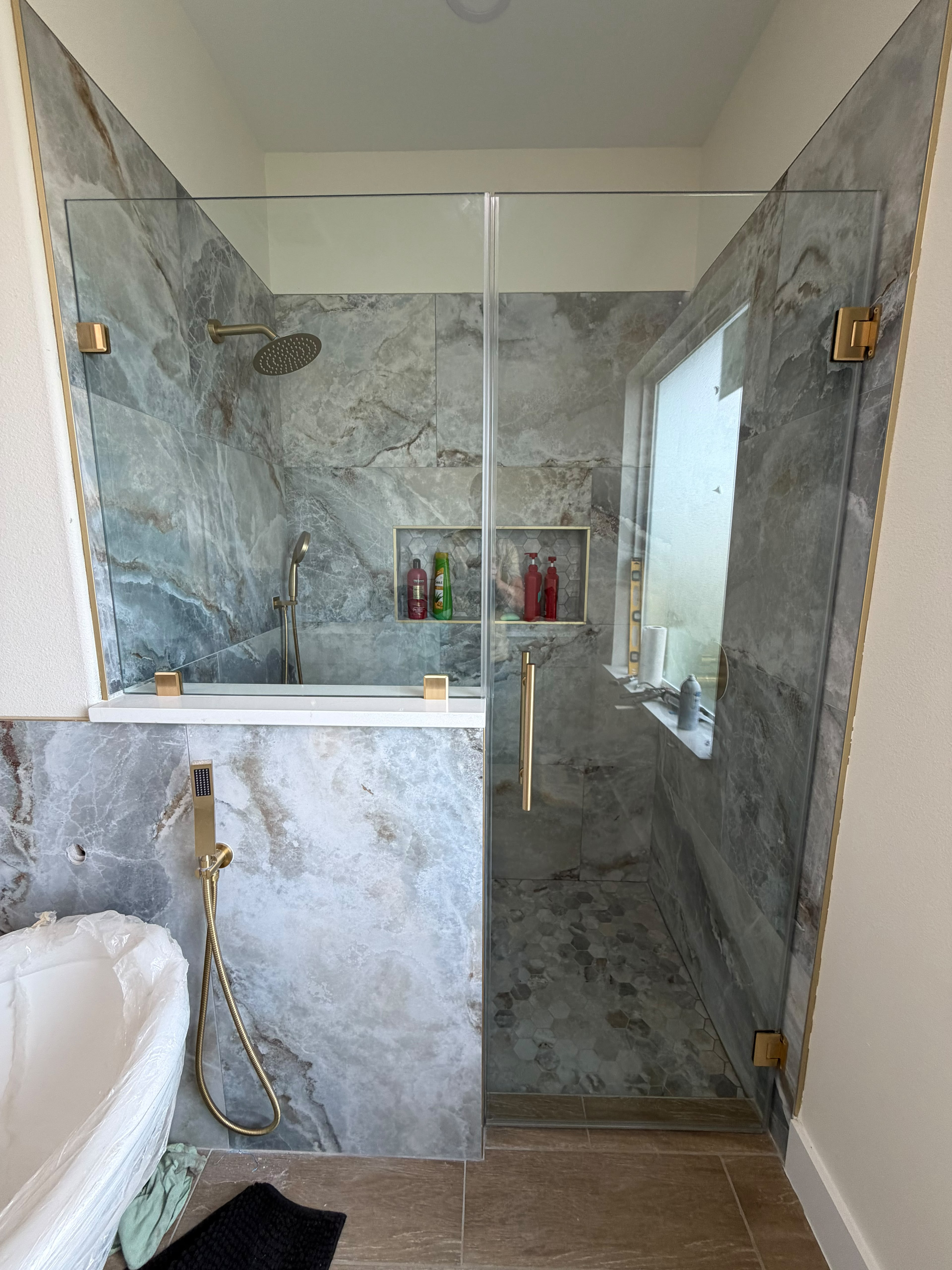 Custom frameless glass shower enclosure over pony wall with satin gold hardware