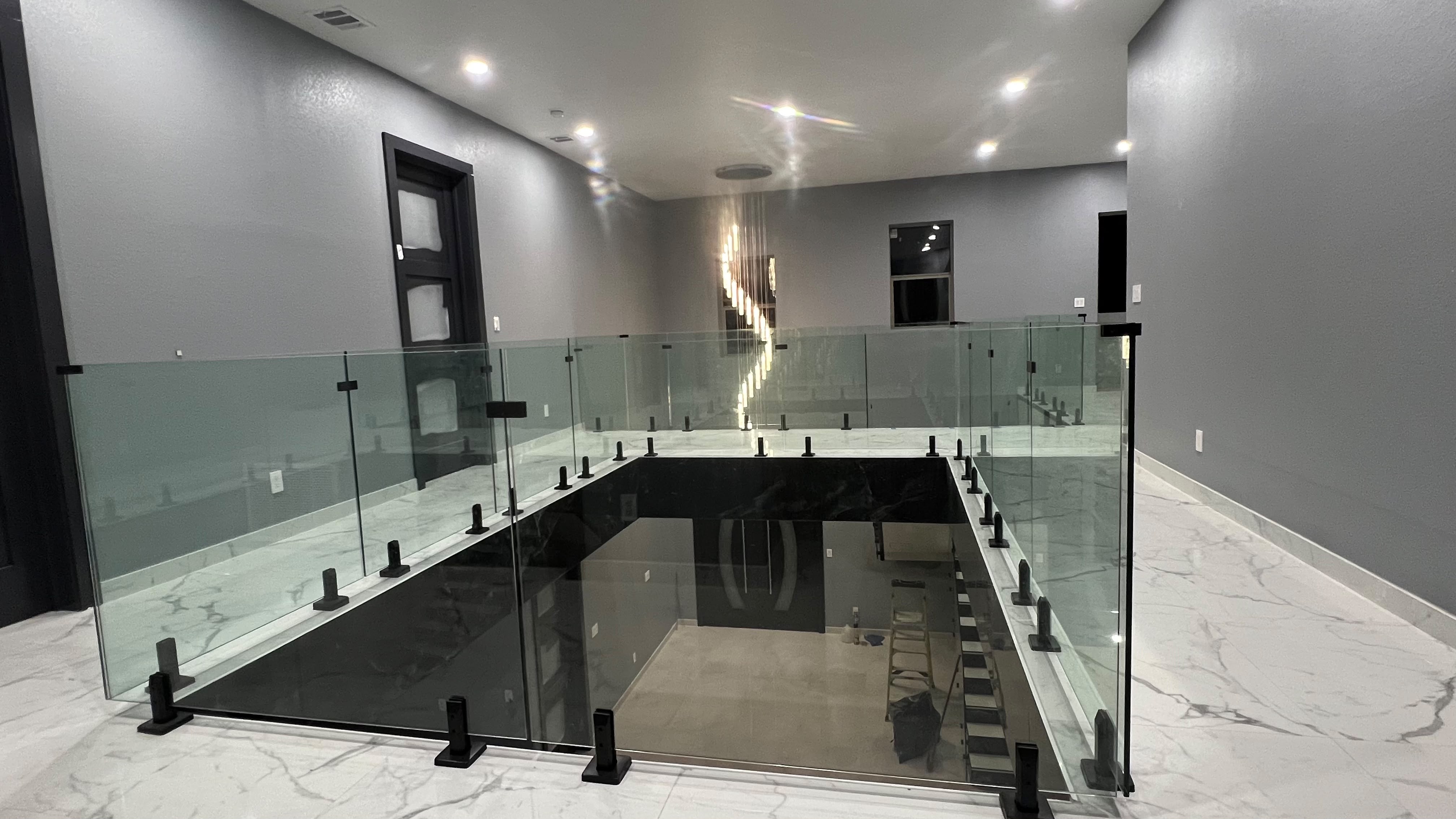 Upper floor frameless glass mezzanine railing overlooking foyer with black floor spigots