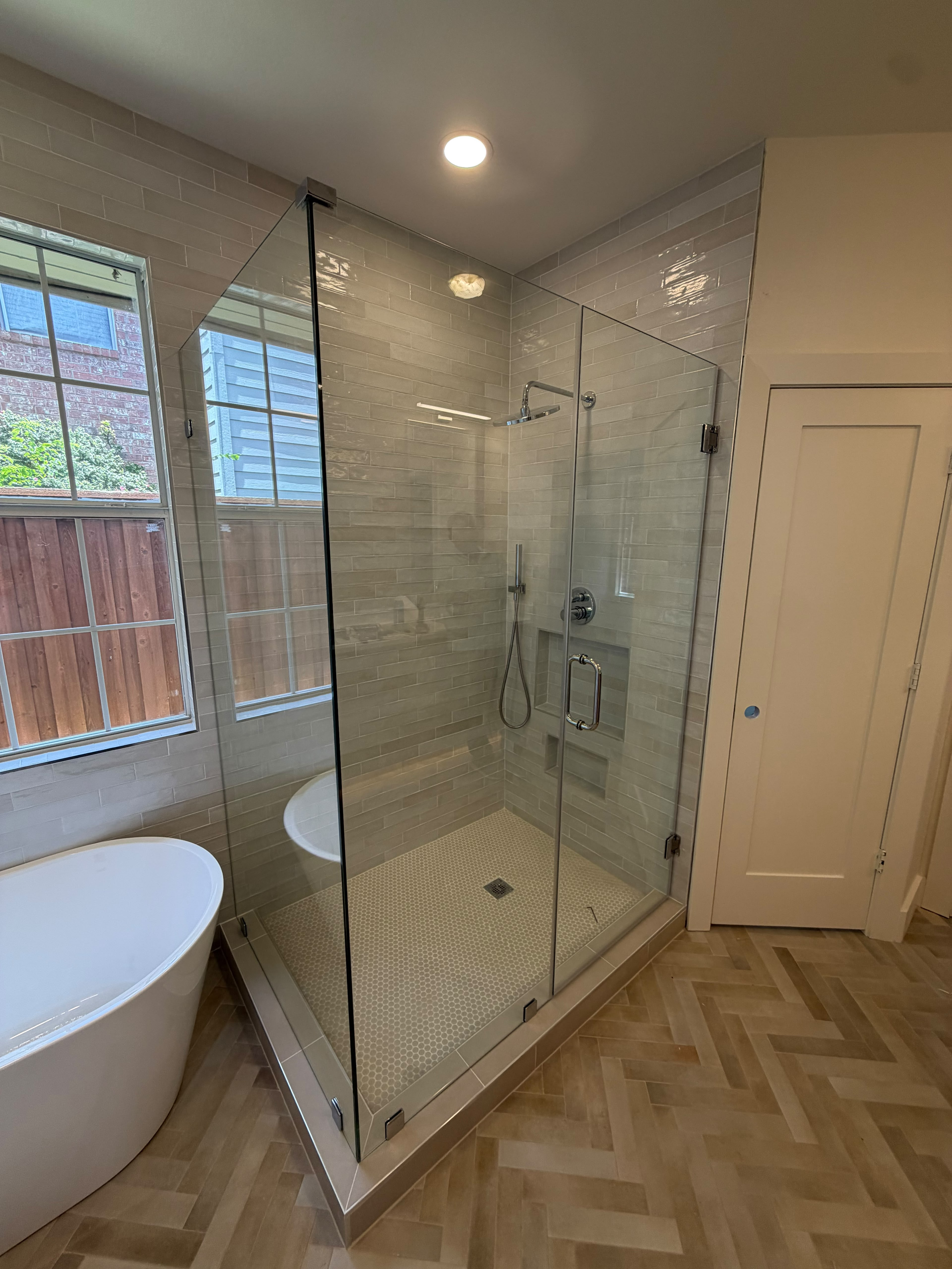 Custom corner glass shower enclosure adjacent to freestanding bathtub with polished chrome hardware