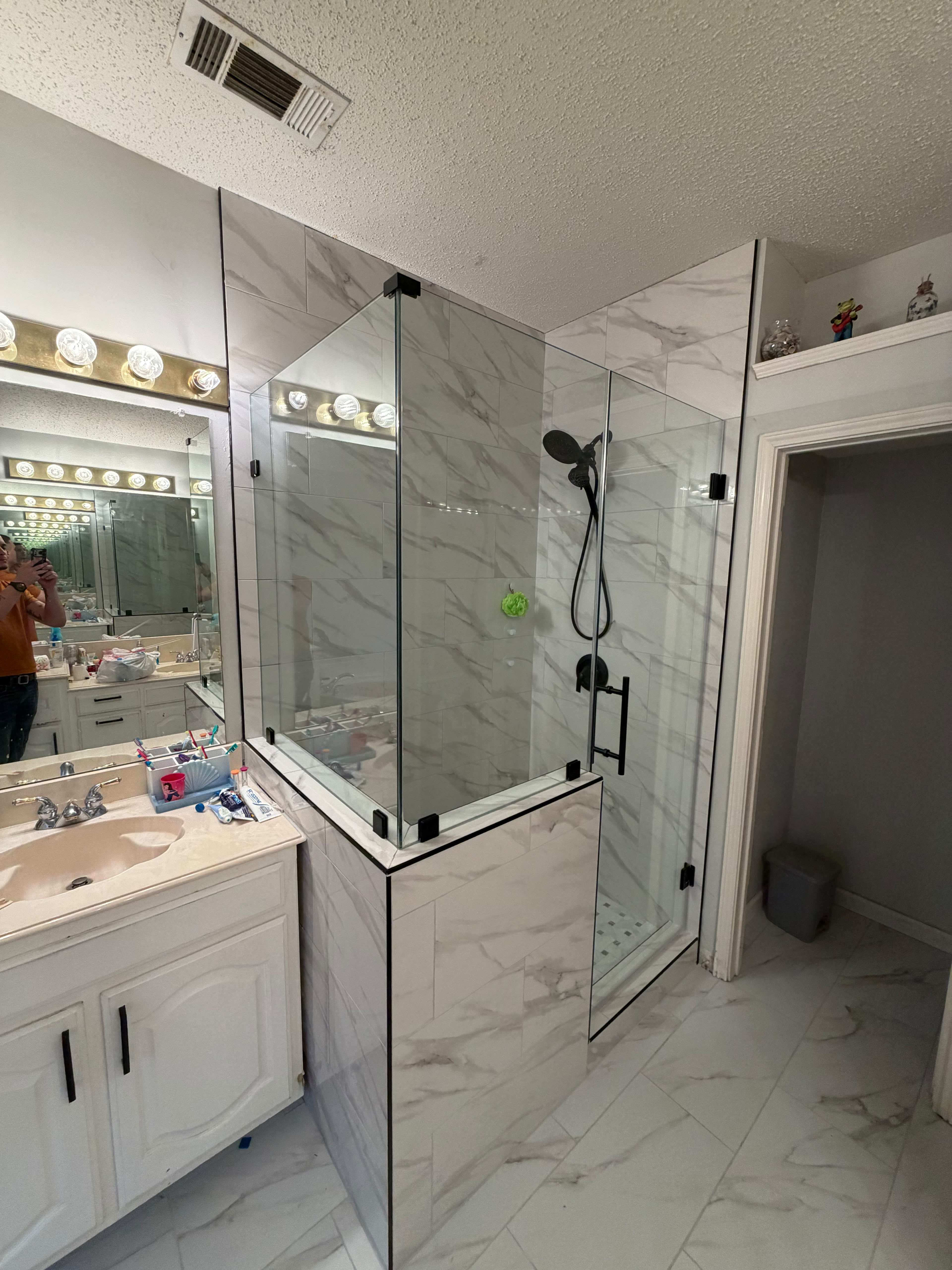 Frameless neo-angle glass shower enclosure with matte black hardware on pony wall