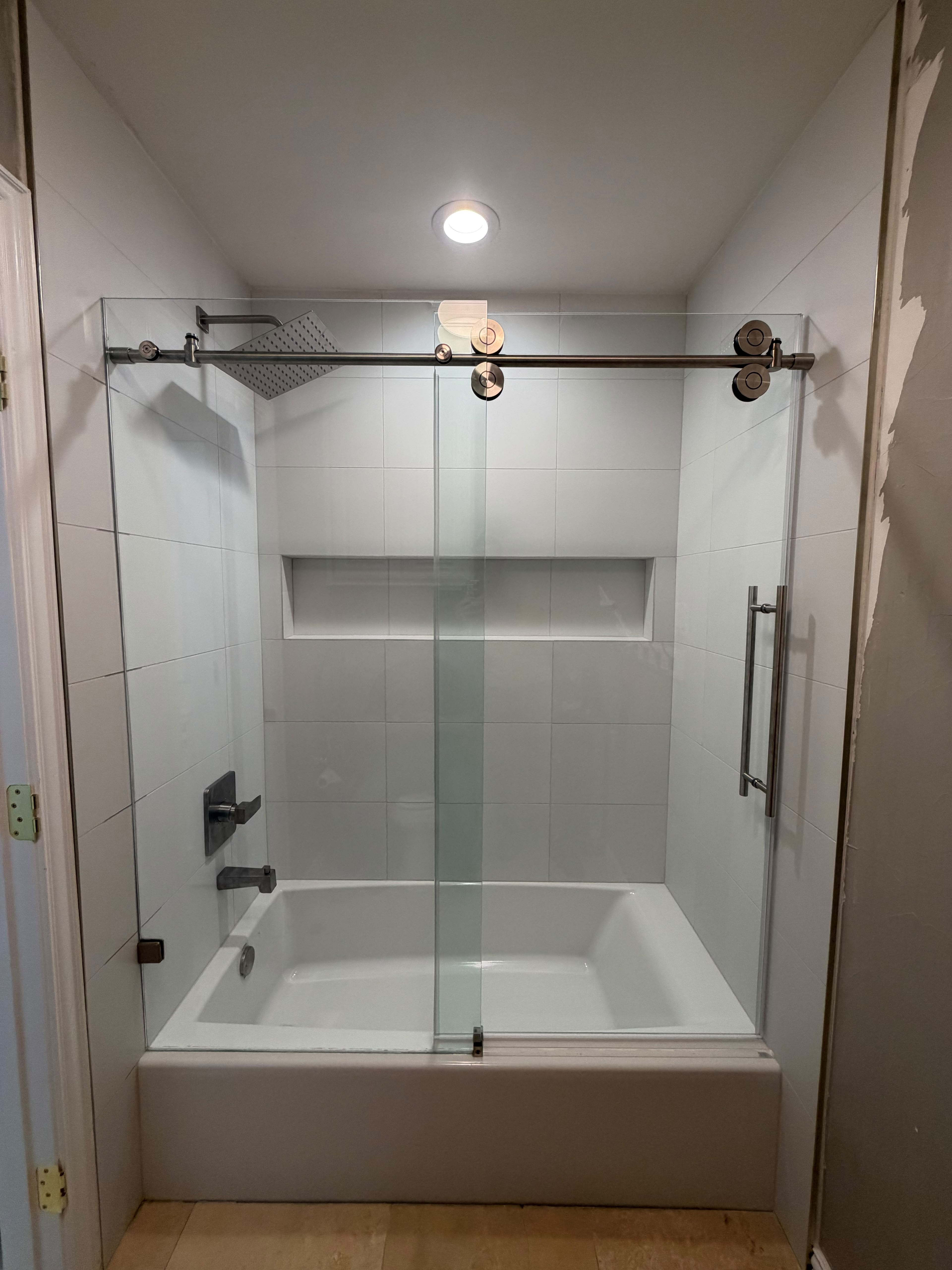 Modern frameless sliding glass barn door shower over bathtub with brushed nickel rollers