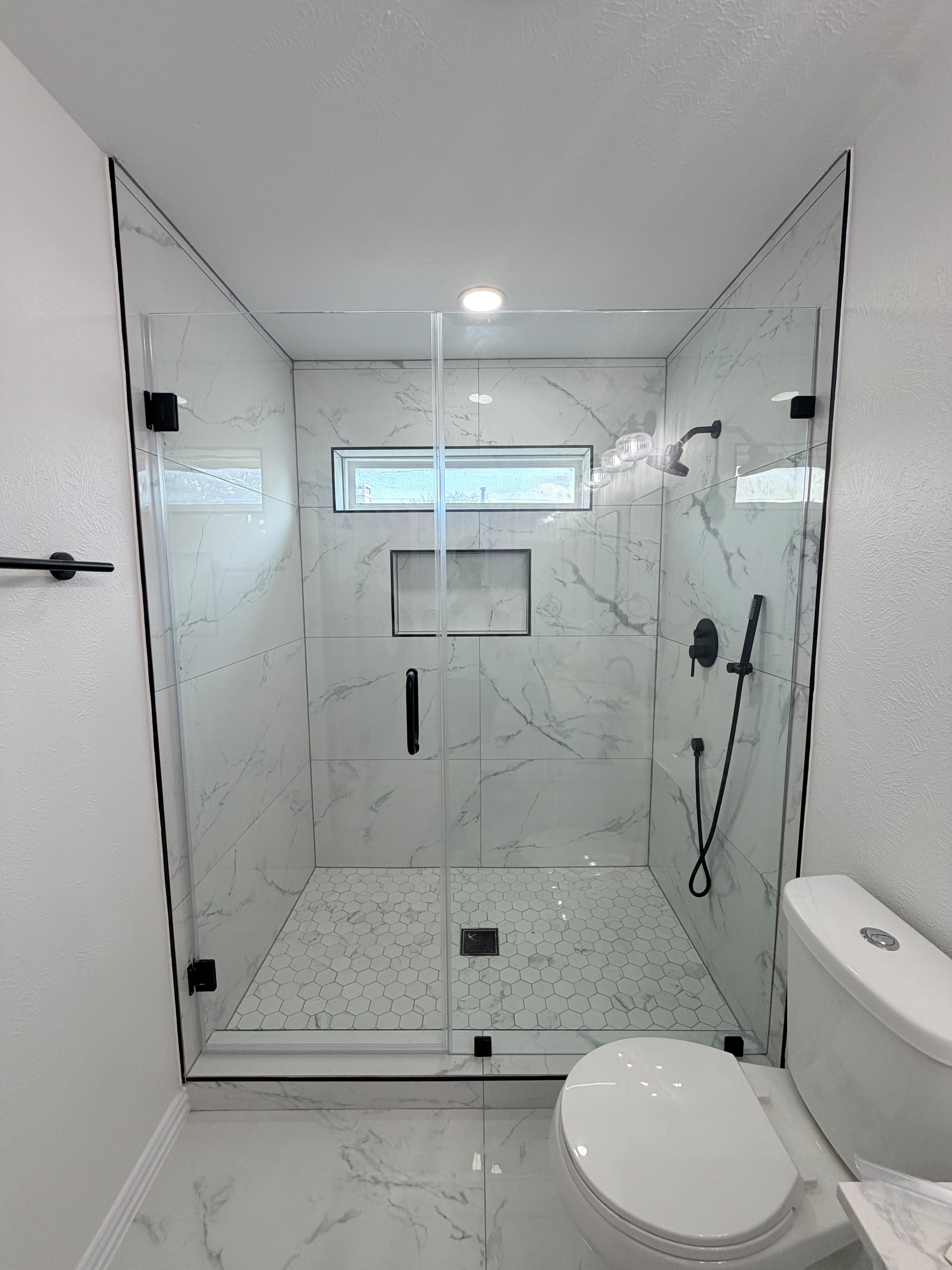 Custom frameless glass shower enclosure with matte black hardware and white marble tile