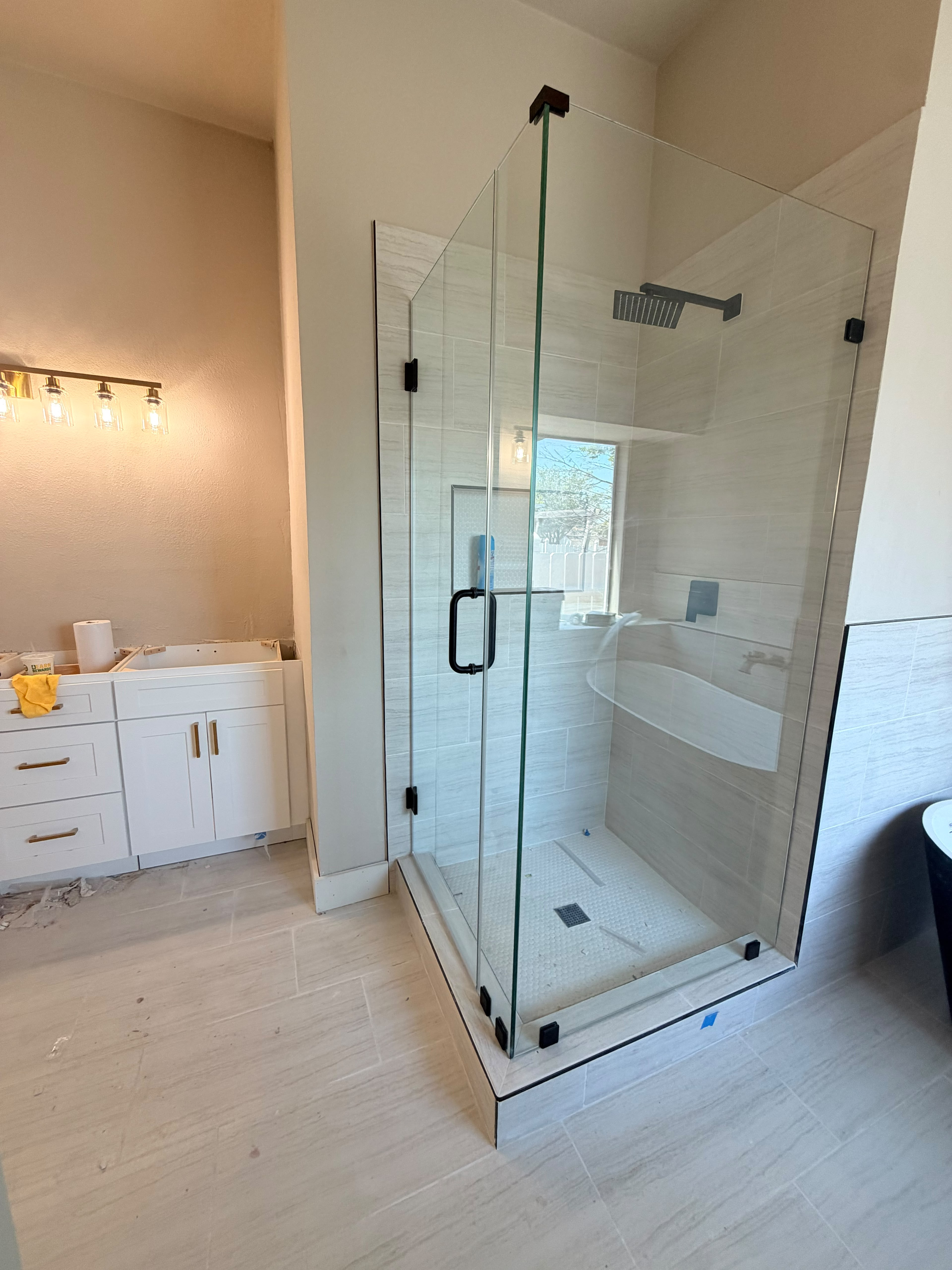 Custom corner frameless glass shower enclosure with black hardware and tiled base