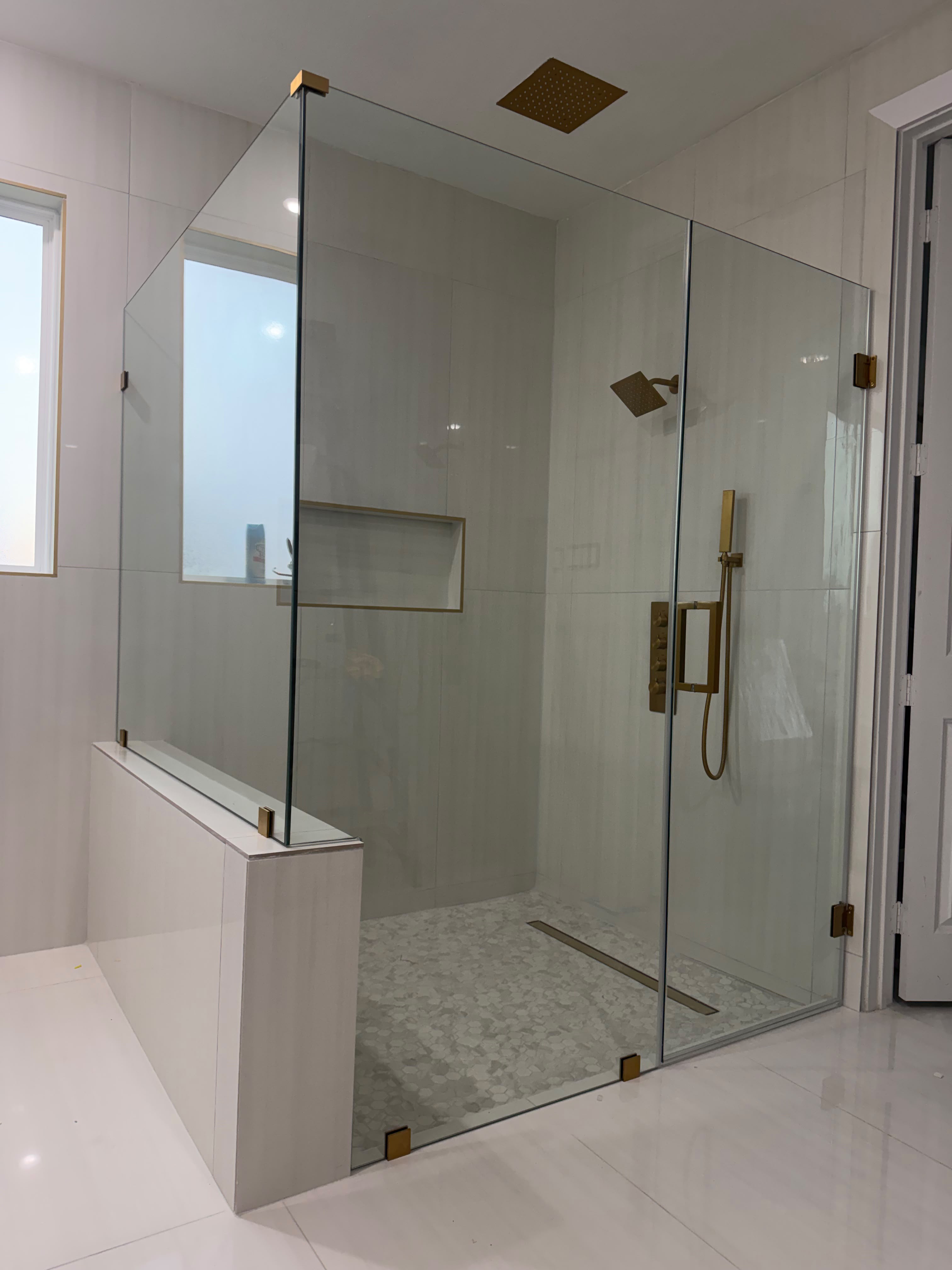 Luxury frameless glass shower enclosure with brushed gold hardware on half wall