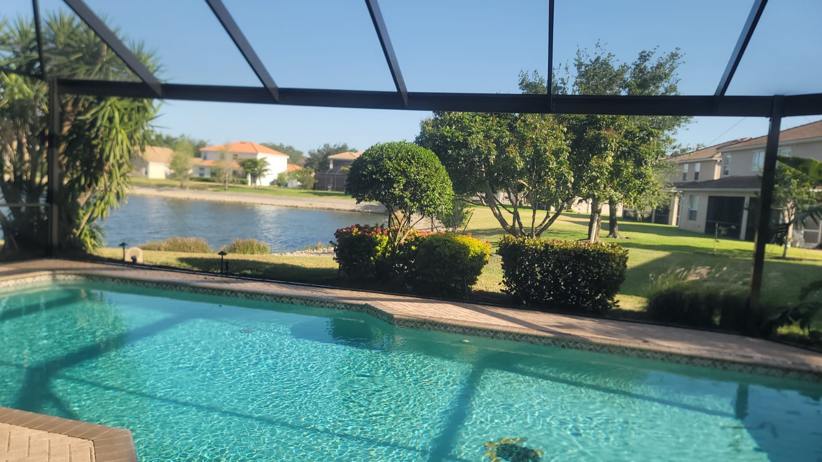 Crystal-clear view looking out over lake, water, and landscaping through Excel Exteriors pool enclosure screen in Southwest Florida