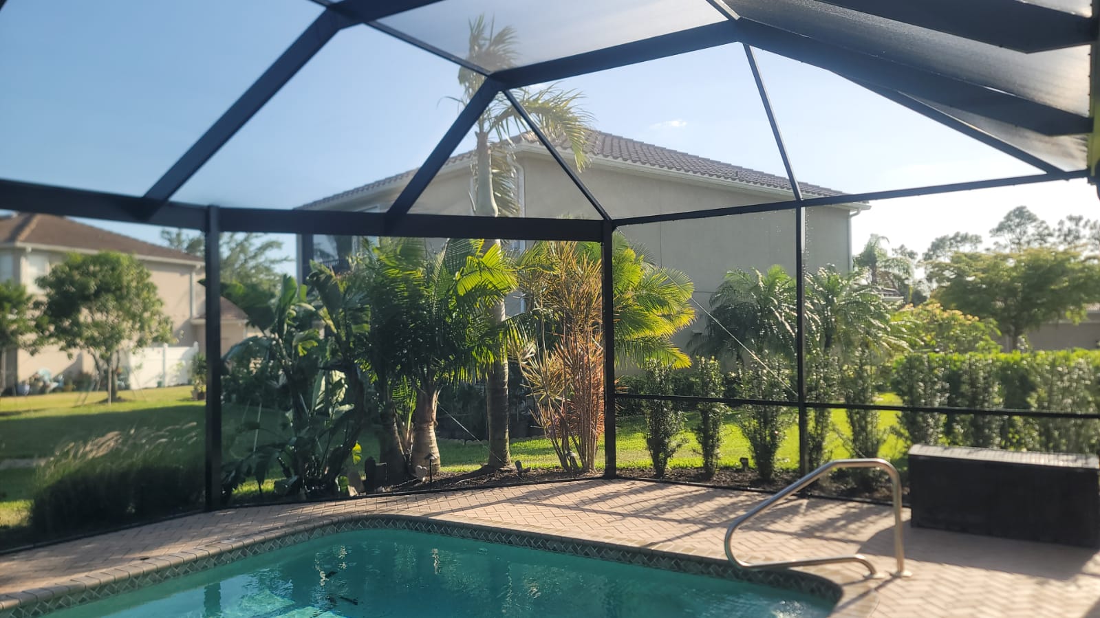 Patio with swimming pool, pavers, and palm trees under custom enclosure overlooking Southwest Florida backyard