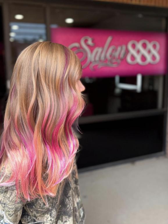 Salon 888 client with vibrant pink peek-a-boo highlights under blonde waves