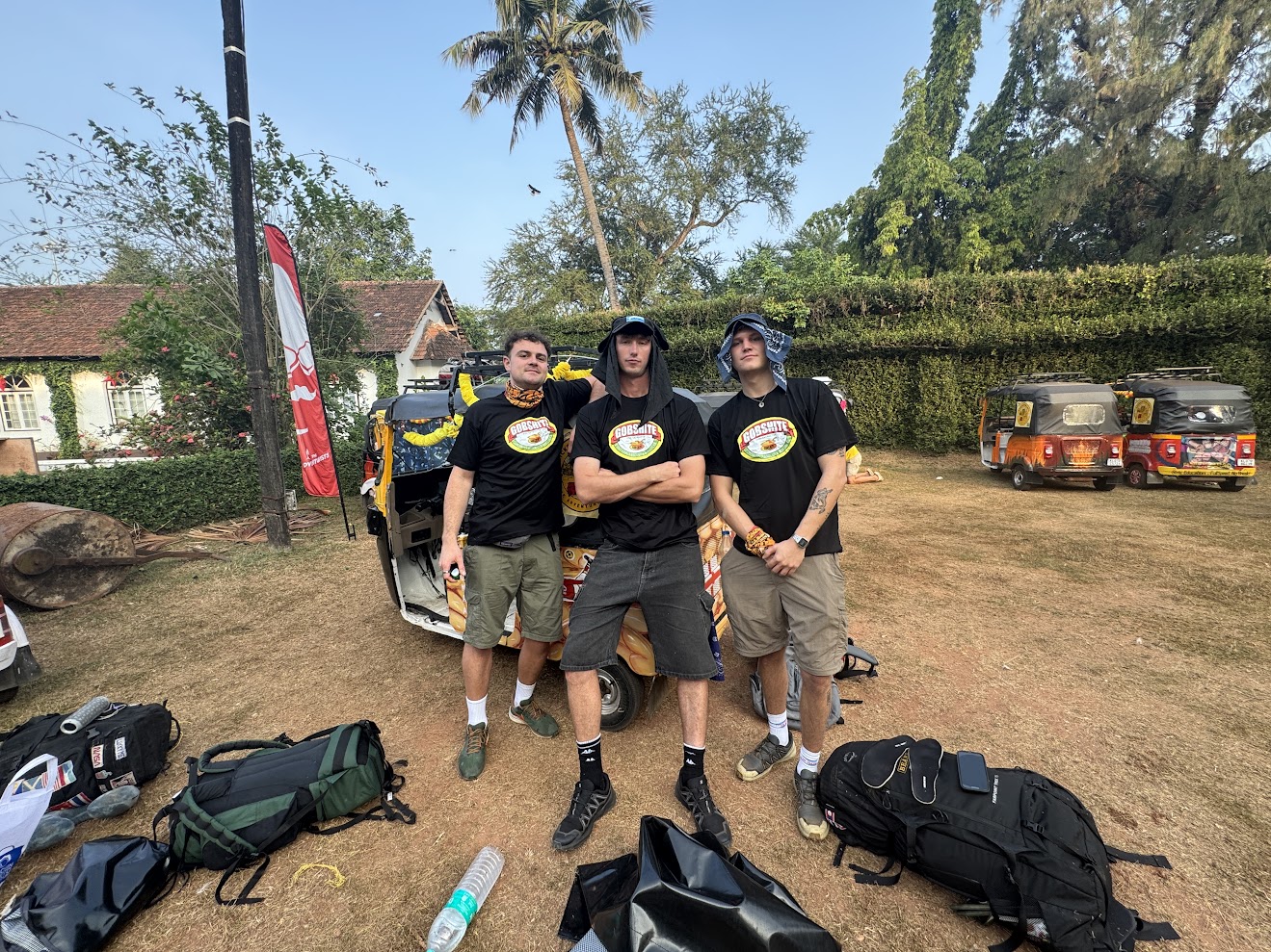 Three young men standing together in front of a rickshaw with expedition backpacks and gear