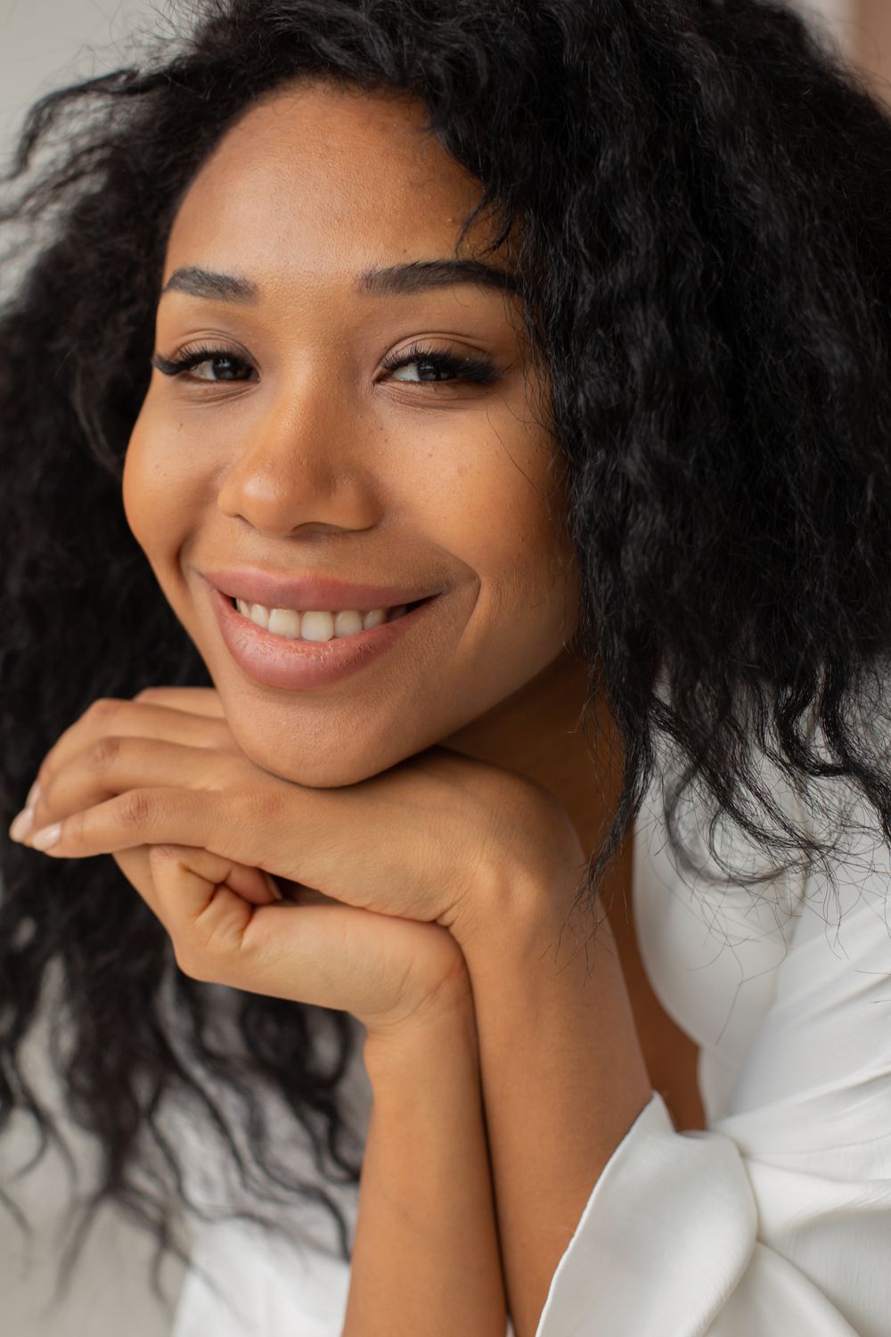 Editorial portrait of a woman smiling with her chin resting on her hands.