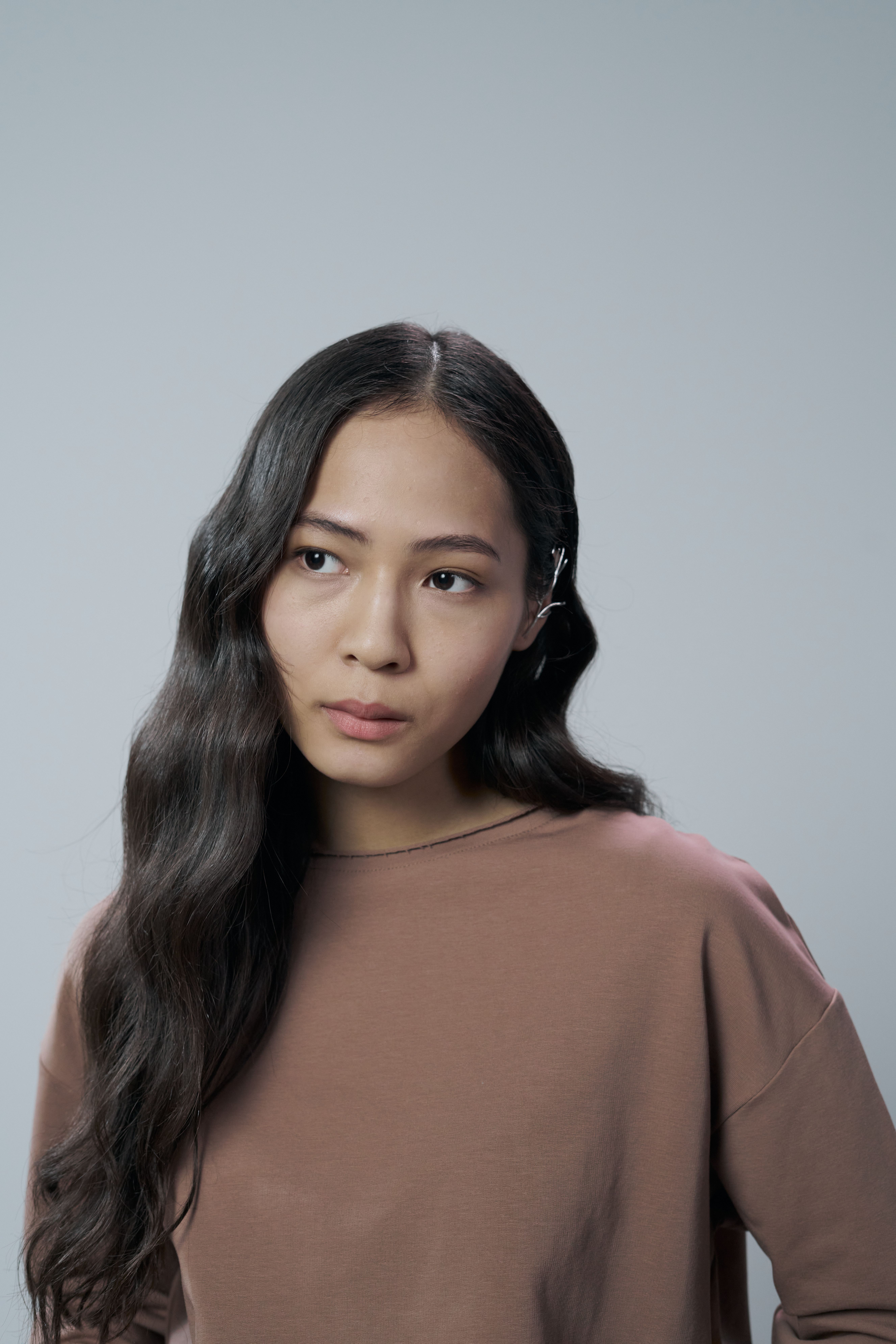 Editorial portrait of a woman with long dark hair against a blue-gray background.