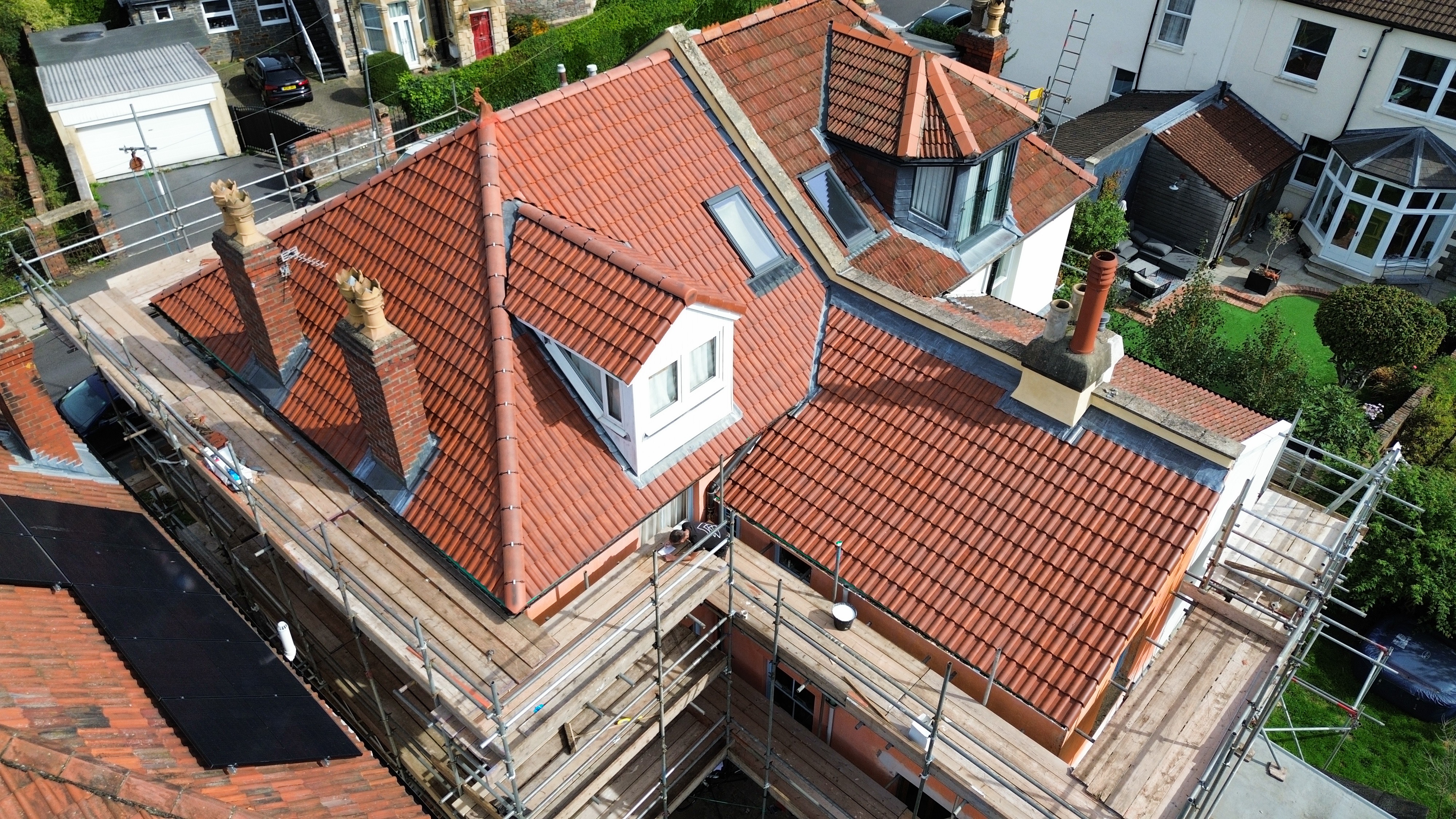 Aerial Inspection: Angled drone view assessing interlocking roof tiles, lead valleys, dormer junction and roofer inspection.