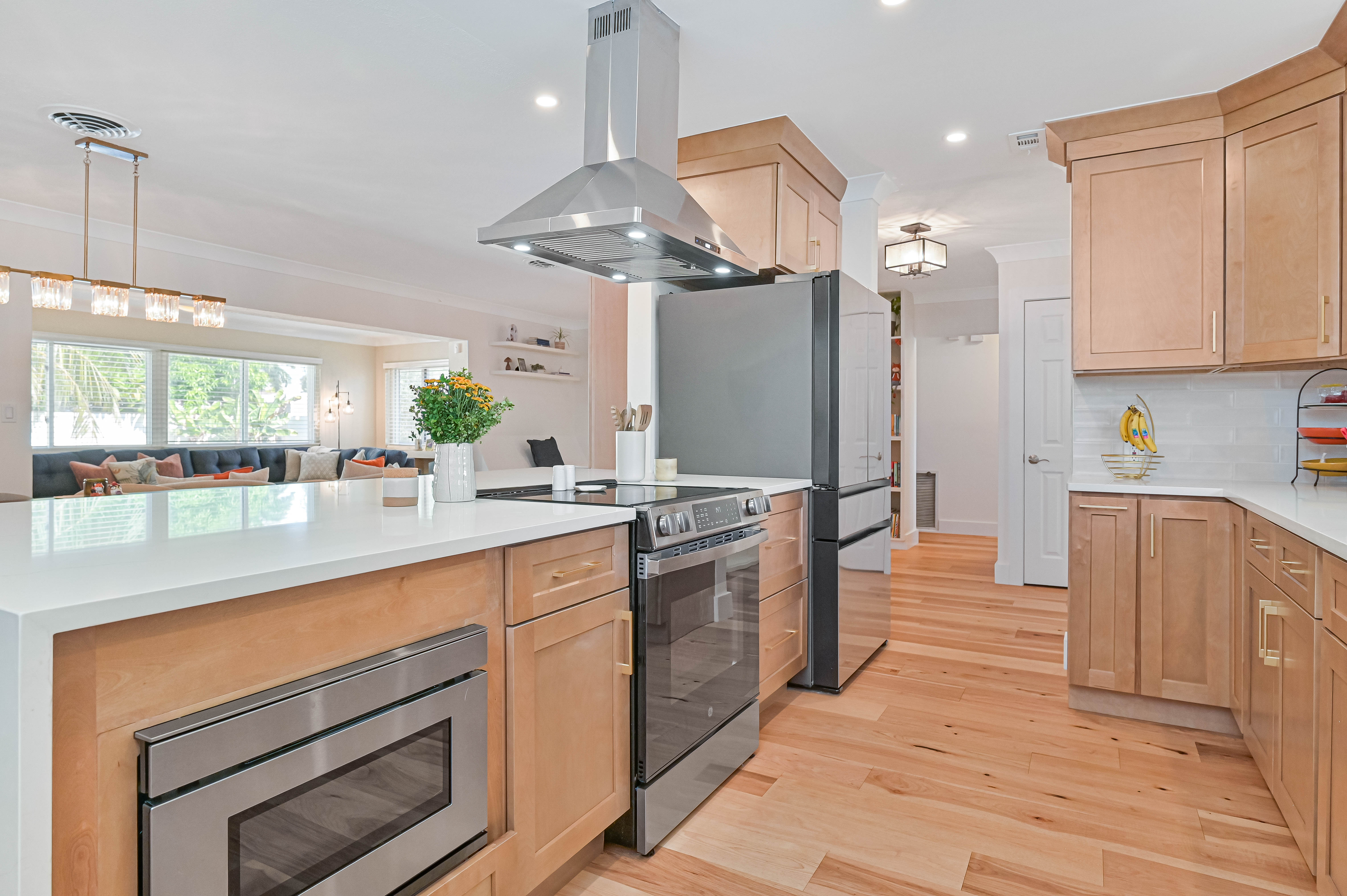 Schooner Bay Builders kitchen island with built-in microwave drawer, slide-in range, stainless vent hood, and light wood cabinetry