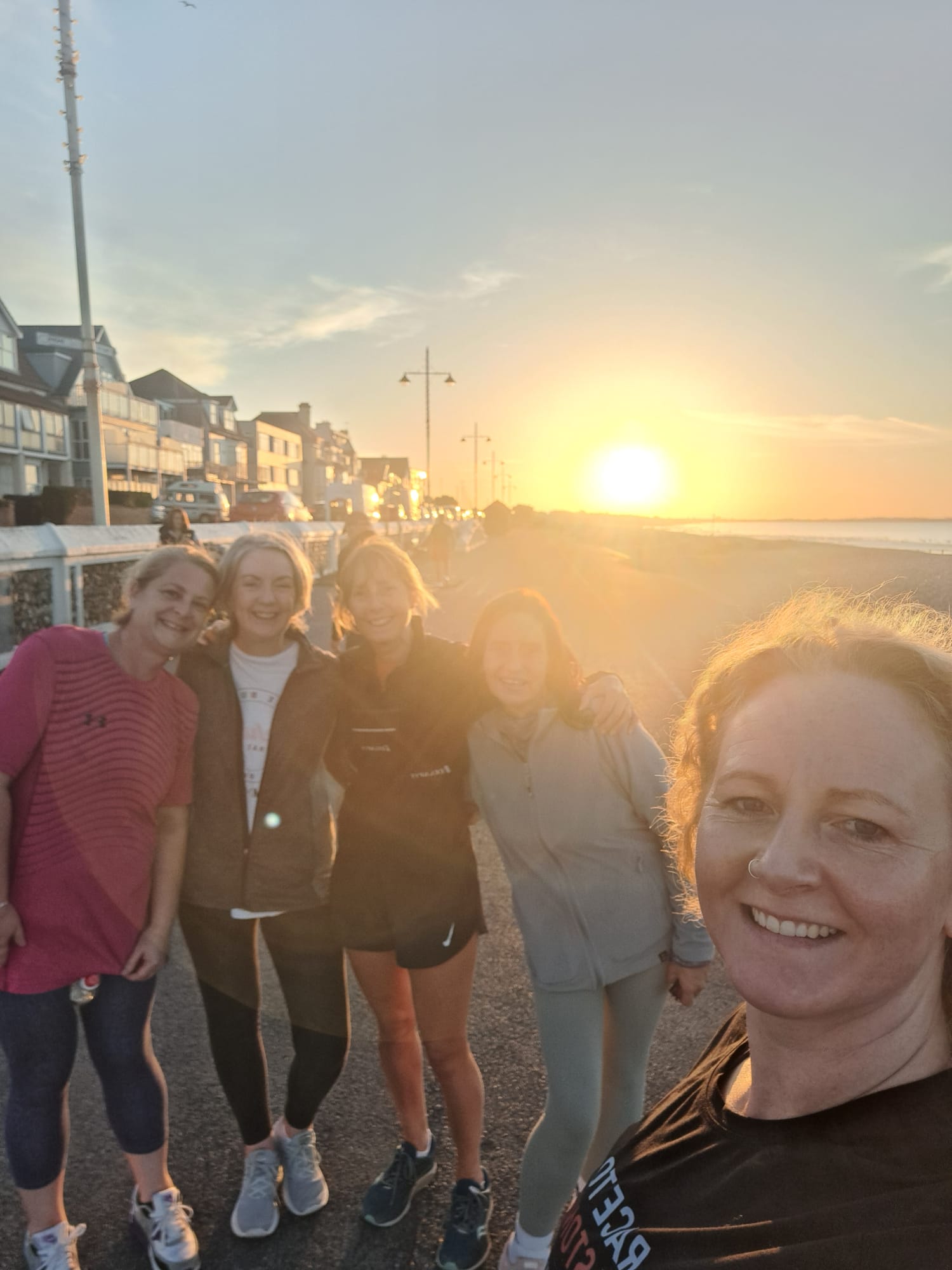 LukeMurray.Fit members smiling together during an outdoor run at sunset along the Bognor Regis seafront