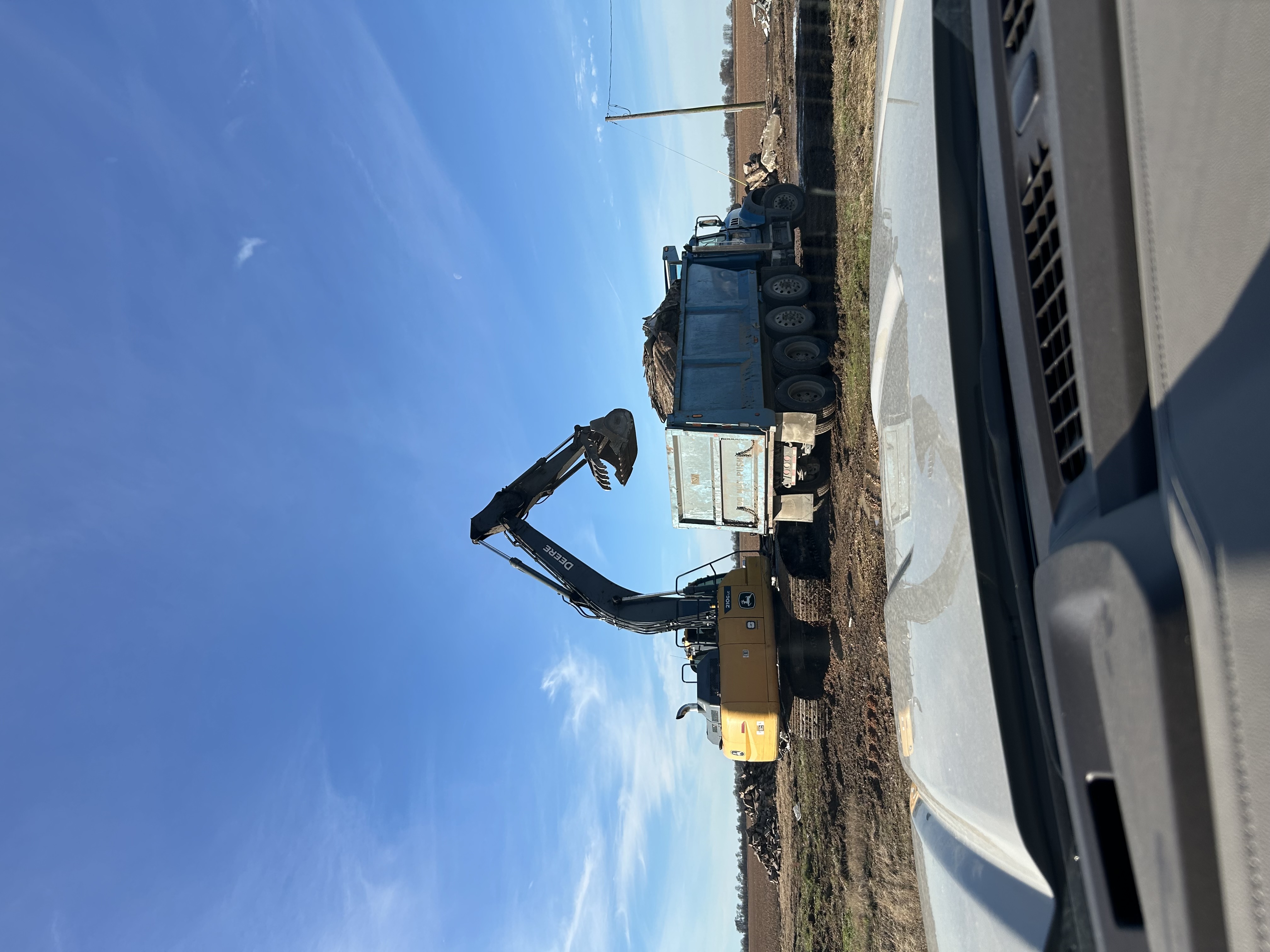 John Deere 210G excavator loading haul truck on ditch remediation job
