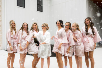 Bride and bridesmaids celebrating and popping champagne outdoors with champagne foam spray