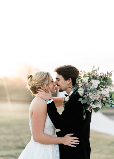 Bride and groom sharing an intimate embrace with winter floral bouquet featuring blue thistle and eucalyptus