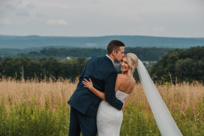 Groom kissing bride's forehead in a scenic summer meadow overlooking the Laurel Highlands