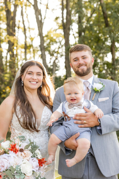 Bride and groom with baby in autumn woodland setting at The Willow
