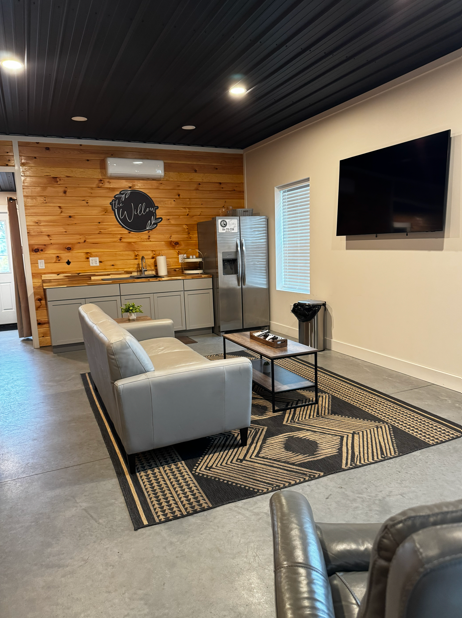 Groom's Den lounge at The Willow with leather sofa, wall-mounted television, and kitchenette prep area