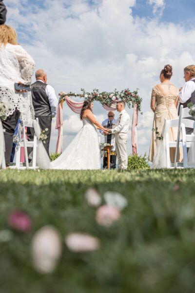 Couple holding hands at wedding ceremony altar framed by floral arbor and blue sky
