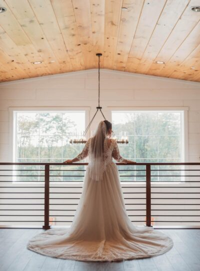 Bride in lace wedding gown standing at mezzanine railing looking out the grand windows