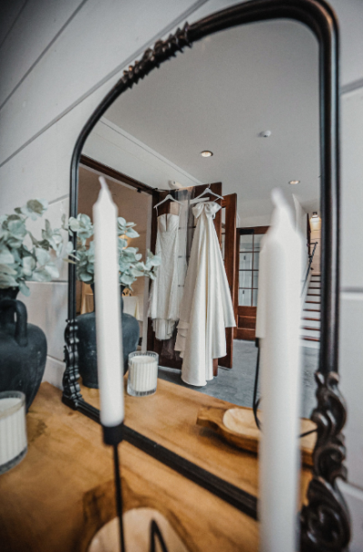 Framed mirror reflection of wedding dresses hanging in doorway with taper candles