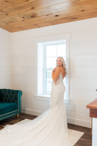Bride standing beside sunlit window in the bridal suite with emerald green chesterfield sofa