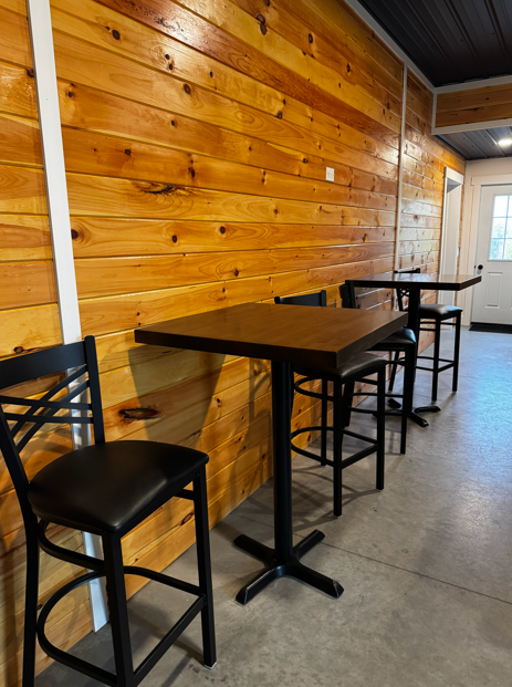 Groom's den pub-height tables and bar seating along natural wood wall at The Willow