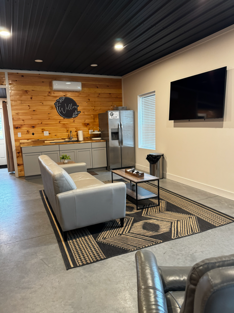 Groom's den lounge with leather couch, coffee table, wall TV, and kitchenette at The Willow