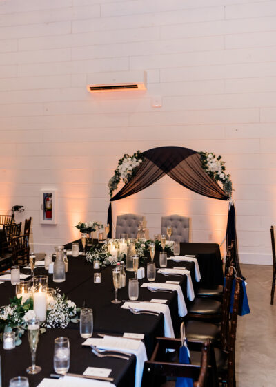 Intimate wedding head table with black linens, candlelit place settings, and draped floral sweetheart arch
