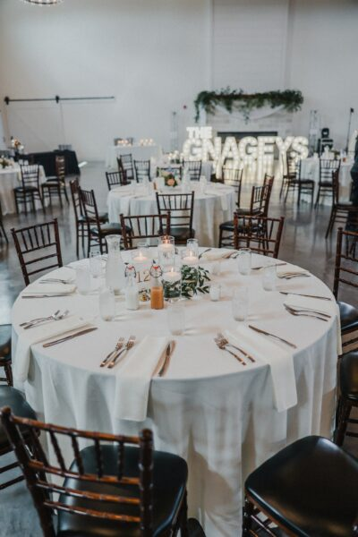 Elegantly set reception table with candles, greenery, and illuminated marquee letters in background