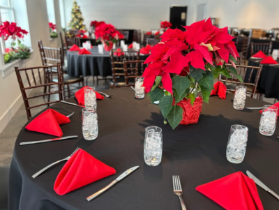 Festive round banquet dining table set with vibrant red poinsettia centerpieces and folded red napkins in the Side Room