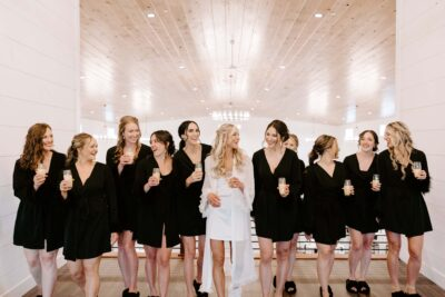 Bride in white robe and bridesmaids in black robes toasting champagne across the mezzanine balcony