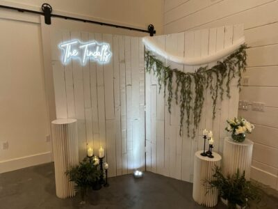 Custom neon sign photo backdrop with white shiplap wall, draped garland, and candlelit pedestals