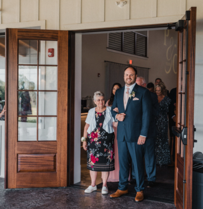 Groom escorting mother through wood double doors onto the patio ceremony area