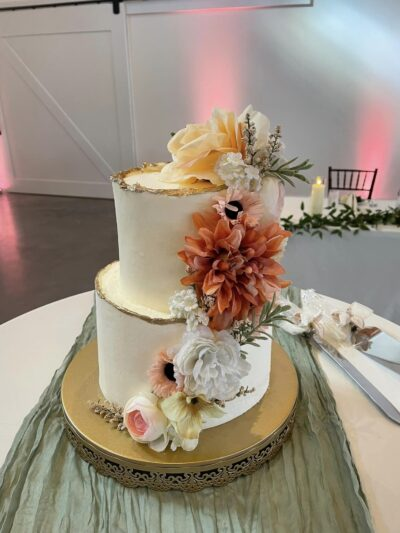 Two-tiered wedding cake with gold foil rim and autumn dahlias and roses
